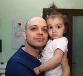 Bărbat cu părul ras care ține o fetiță cu părul lung în brațe, amândoi zâmbind.