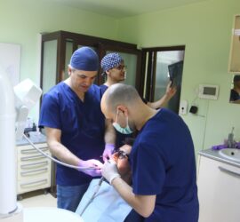 Doi medici dentiști efectuează o consultație dentară asupra unui pacient într-un cabinet.