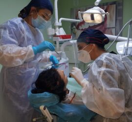 Două asistente stomatologice efectuează o procedură pe un pacient într-o clinică dentară.