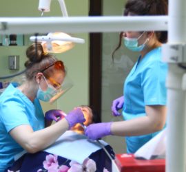 Două asistente dentare efectuează o procedură pe un pacient într-un cabinet stomatologic.