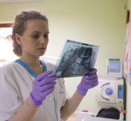 Asistentă dentară cu mănuși violet examinând o radiografie dentară într-un cabinet stomatologic.