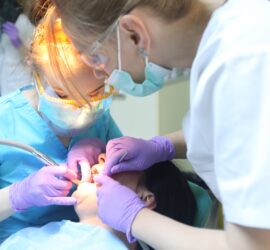Două asistente stomatologice efectuează o procedură pe un pacient în cabinetul stomatologic.