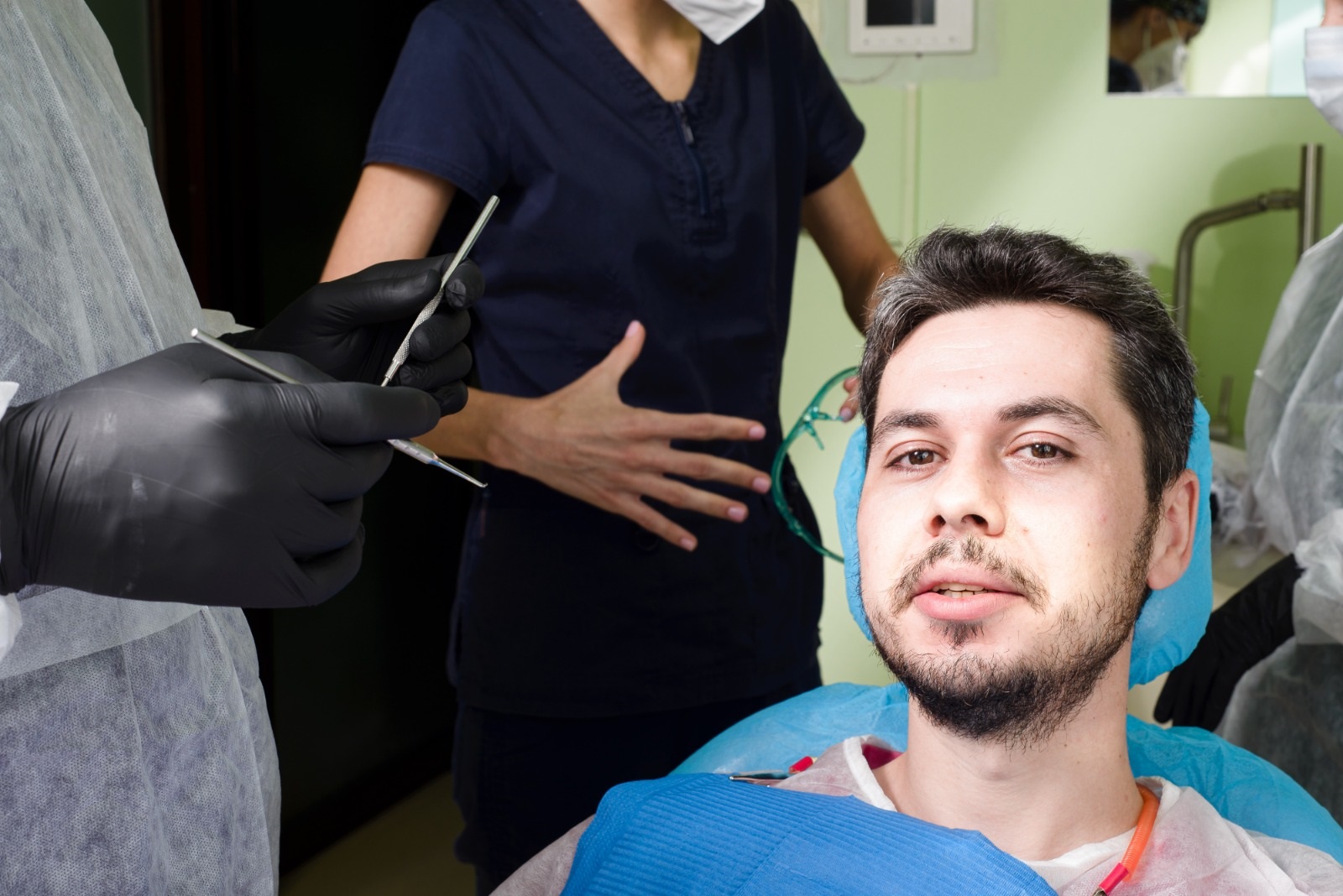 Pacient zâmbind în timp ce se află pe un scaun stomatologic, cu personal medical în fundal.