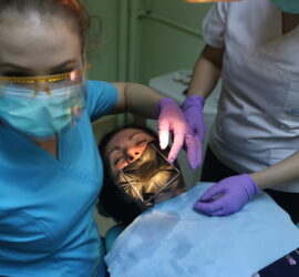 Două asistente stomatologice efectuează o procedură asupra unui pacient în cabinetul dentar.