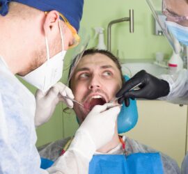 Un pacient în timpul unei proceduri dentare, asistat de doi medici în echipament de protecție.