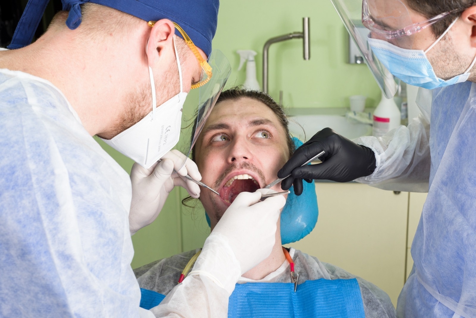 Bacteriile cavității bucale Un pacient în timpul unei proceduri dentare, asistat de doi medici în echipament de protecție.