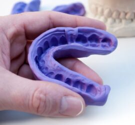 Amprentă dentară din material flexibil de culoare violet, ținută în mână, cu detalii ale dinților vizibile.