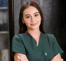 Asistent medical tânăr zâmbind, îmbrăcat în uniformă verde, cu brațele încrucișate.