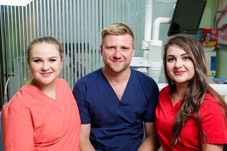 Sistemul imunitar și igiena orală Trei medici dentiști zâmbind în uniformă, în interiorul unei clinici dentare.