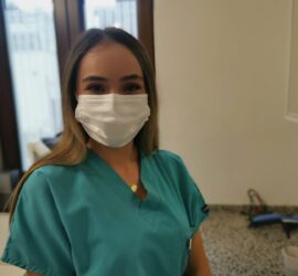 Asistent medical zâmbind în uniformă verde și mască de protecție într-un mediu de lucru.