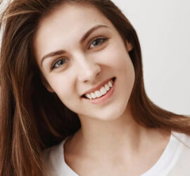 Tânără cu părul lung și zâmbet, purtând un tricou alb, pe un fundal neutru.