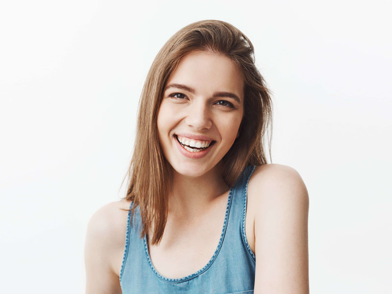 Tânără cu păr lung și drept, zâmbind, purtând un top din denim, pe fundal alb.