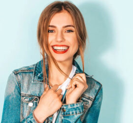 Tânără cu păr lung și blond, zâmbind, îmbrăcată într-o jachetă din denim.