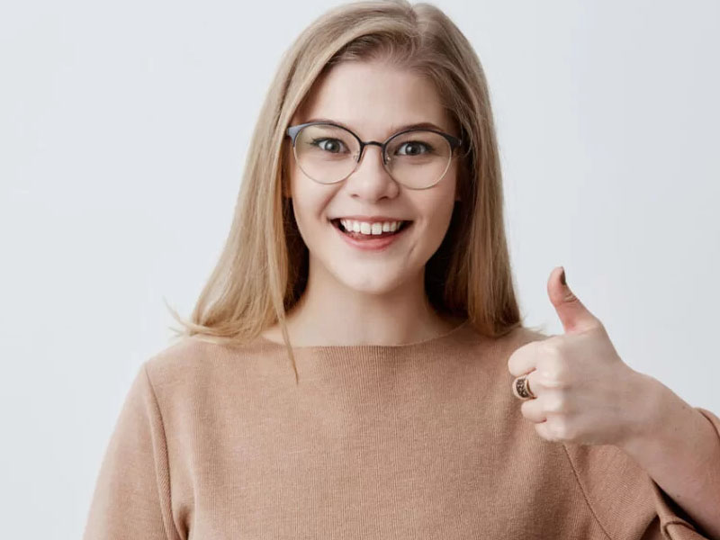 Fată cu ochelari, zâmbind și ridicând degetul mare în semn de aprobat.