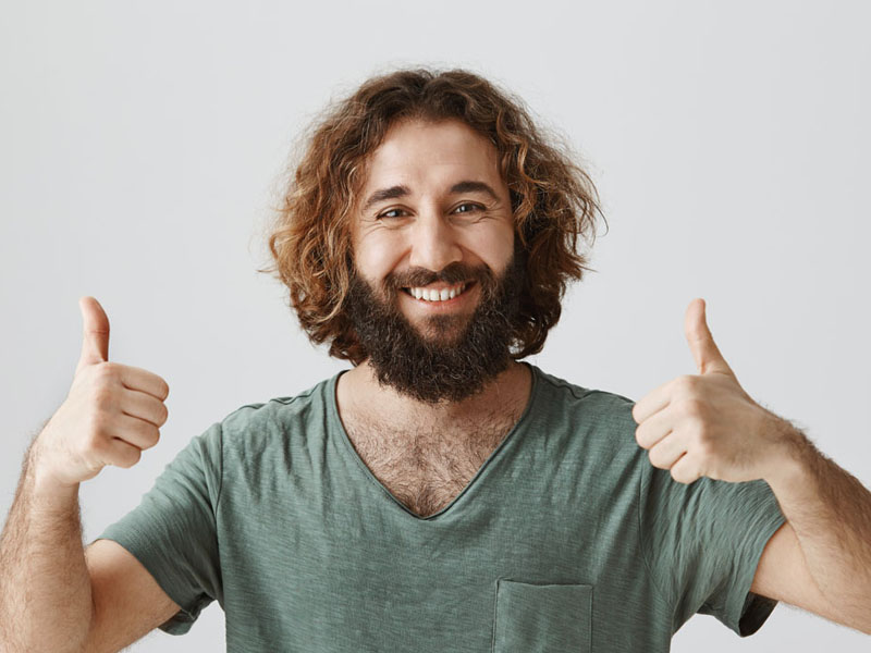 Bărbat cu păr creț și barbă, îmbrăcat în tricou verde, arătând semnul de aprobat cu ambele mâini.