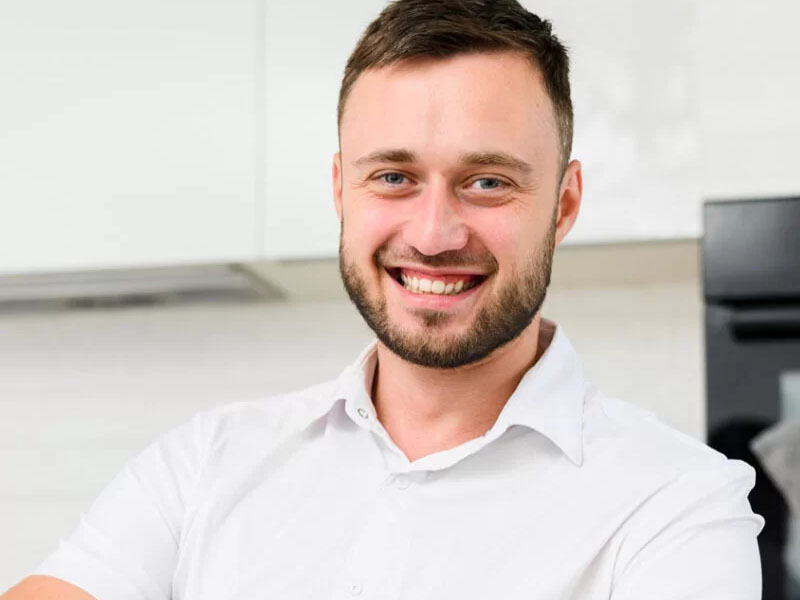 Bărbat tânăr cu păr scurt și zâmbet, purtând o cămașă albă, în interior.