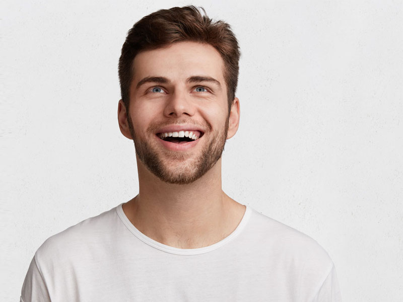 Bărbat tânăr cu păr castaniu și zâmbet larg, purtând un tricou alb.