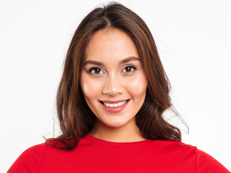 Femeie cu păr lung și ondulat, purtând un tricou roșu și zâmbind în fața camerei.