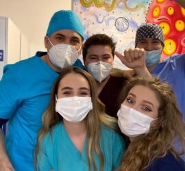 Cinci membri ai unei echipe medicale purtând măști și uniforme, zâmbind în fața camerei.