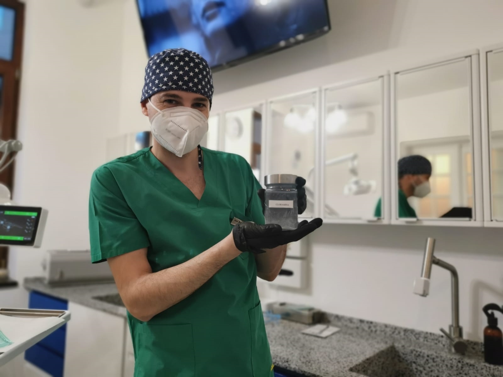 Medic îmbrăcat în uniformă verde, cu mască și mănuși, ținând un recipient în mână.