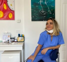 Asistent medical cu părul blond, îmbrăcat în uniformă albastră, stând pe un scaun într-un birou.