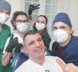 Cinci membri ai echipei dentare pozând împreună, purtând măști și mănuși, în interiorul unui cabinet stomatologic.