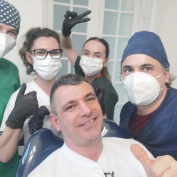 Cinci membri ai echipei dentare pozând împreună, purtând măști și mănuși, în interiorul unui cabinet stomatologic.