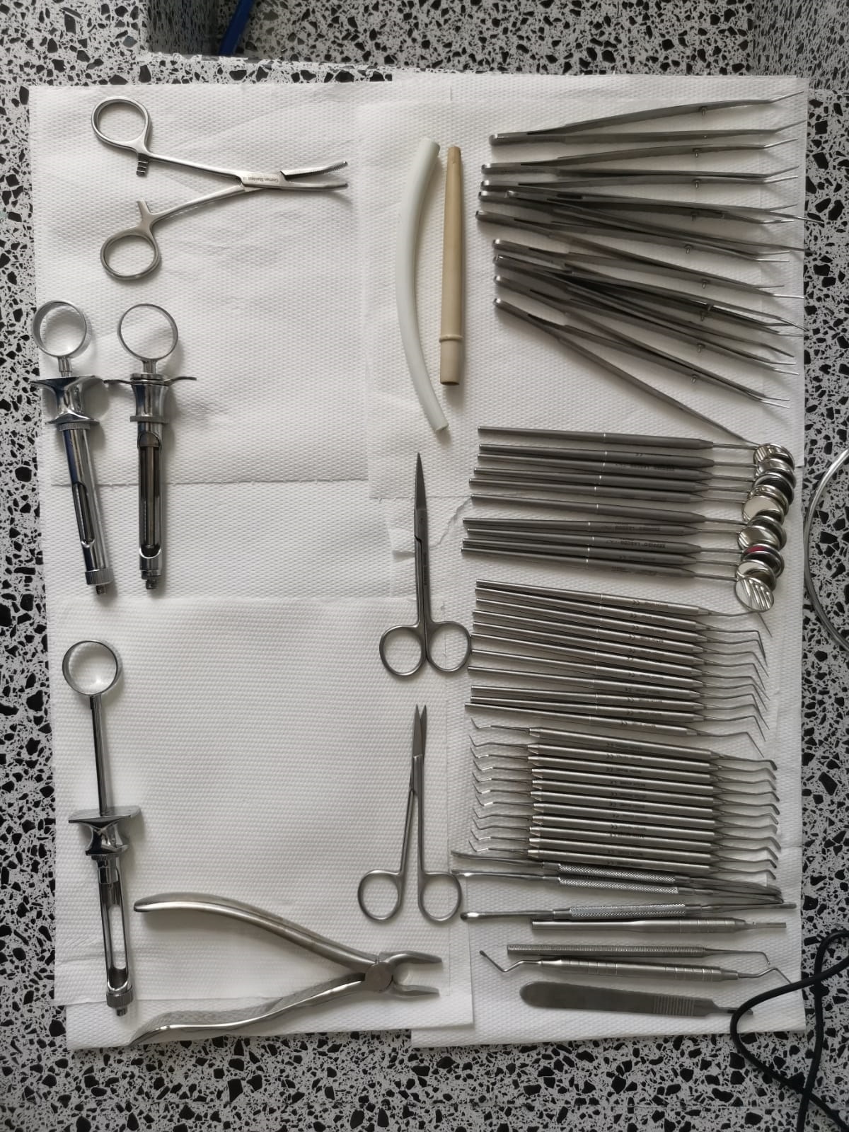 Set de instrumente stomatologice aranjate pe o suprafață albă, inclusiv clești și oglinzi.