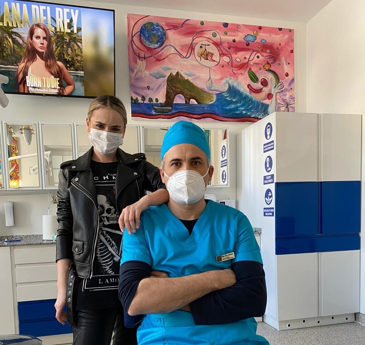 Un medic și un asistent medical, amândoi purtând măști, într-un cabinet medical.