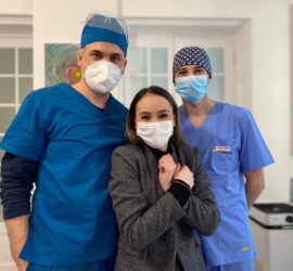 Trei persoane în uniformă medicală, două în albastru și una în gri, toate purtând măști de protecție.