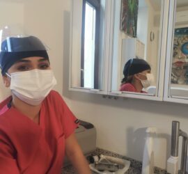 Asistent medical purtând mască și vizieră, zâmbind în fața oglinzii.