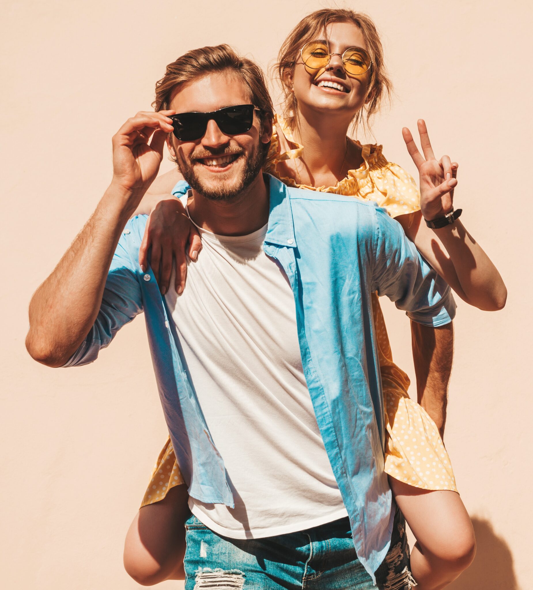 Un bărbat cu ochelari de soare și o femeie zâmbitoare care face semnul păcii, pozând împreună.