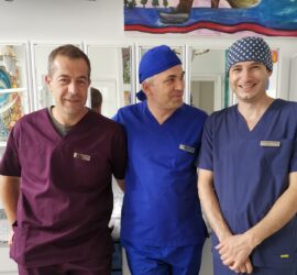 Trei medici îmbrăcați în uniforme de spital, zâmbind în fața camerei.