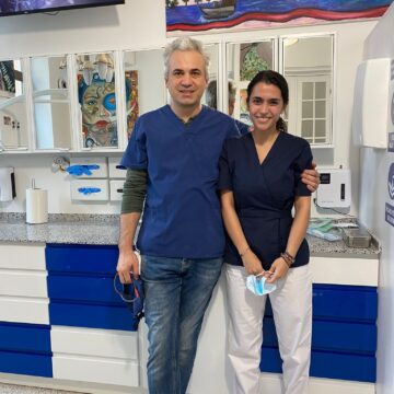 Două persoane îmbrăcate în uniforme medicale stând într-un cabinet stomatologic.