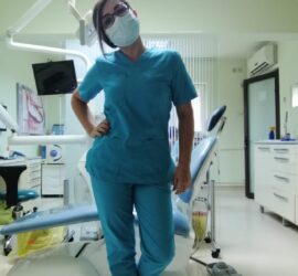 Persoană în uniformă medicală albastră, purtând mască, într-un cabinet stomatologic.