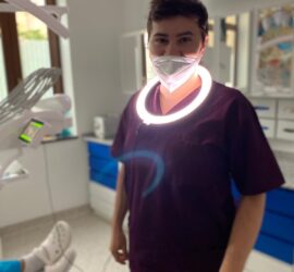 Medic stomatolog purtând o mască și un inel de lumină în jurul gâtului, în cabinetul dentar.