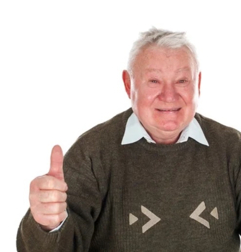 Bărbat în vârstă cu părul alb, zâmbind și arătând degetul mare ridicat, îmbrăcat într-un pulover gri.