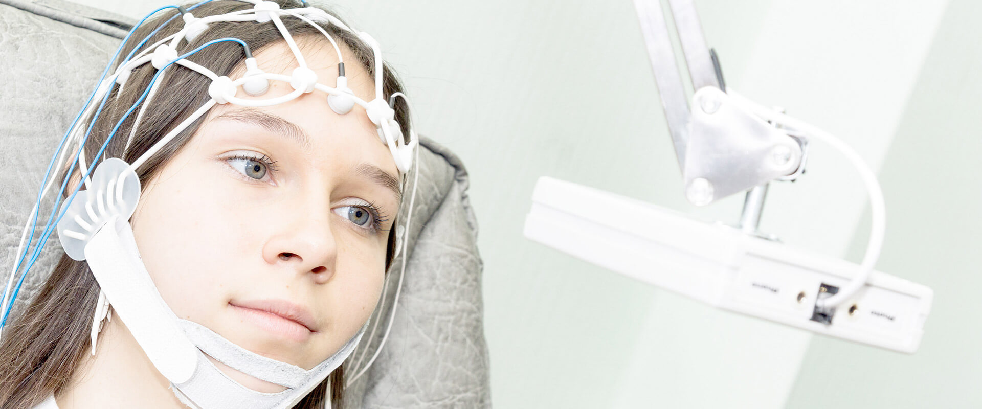 Tânără cu electrozi pe cap, supusă unei electroencefalograme într-un mediu clinic.