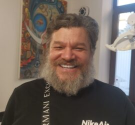 Bărbat cu barbă căruntă și zâmbet larg, purtând un tricou cu logo NikeAir.