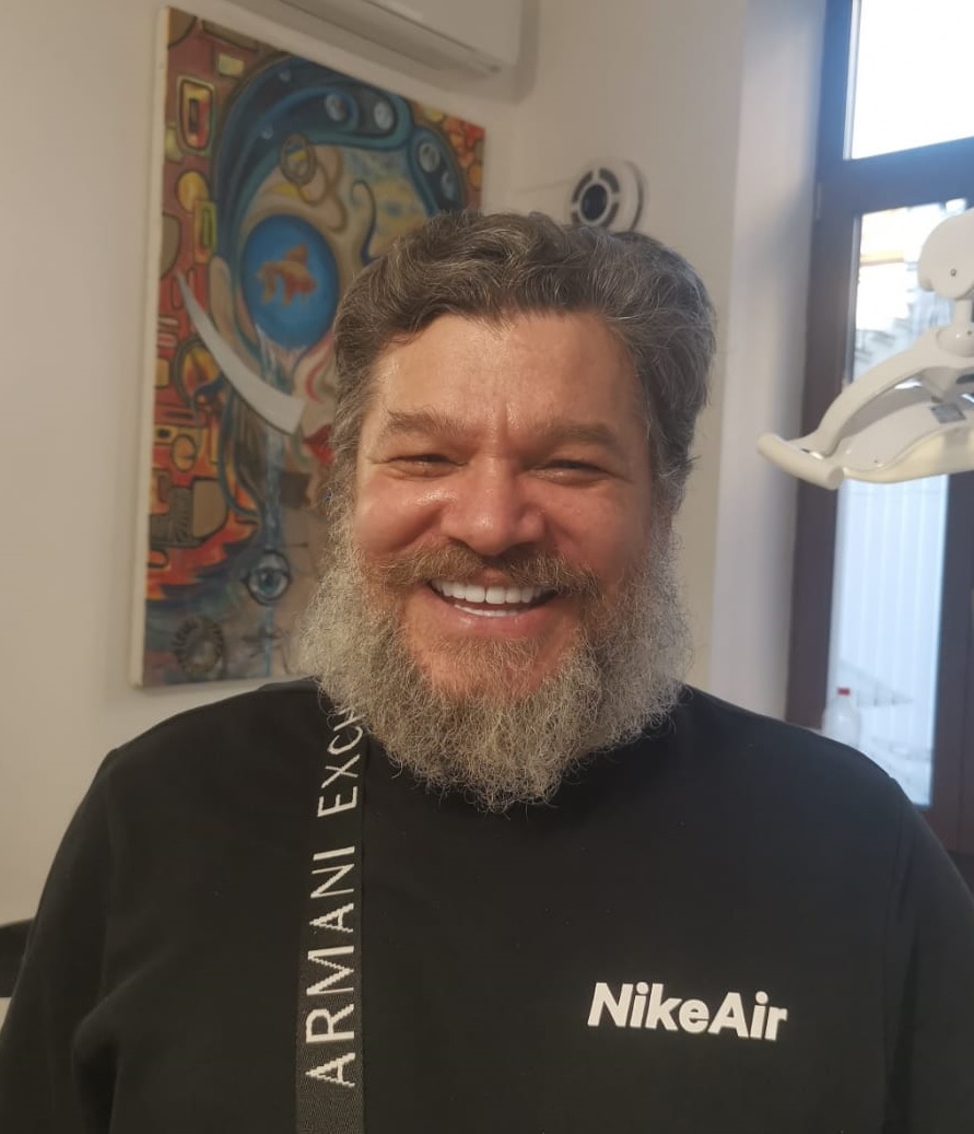 Bărbat cu barbă căruntă și zâmbet larg, purtând un tricou cu logo NikeAir.