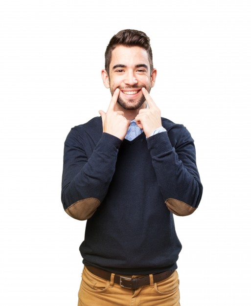 Bărbat tânăr cu părul brunet, zâmbind și arătând cu degetele spre obraje.