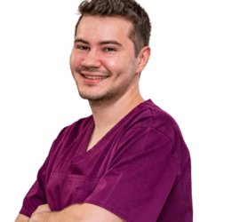 Medic stomatolog zâmbind, purtând un halat de culoare mov, cu brațele încrucișate.