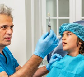 Medic dentist cu mănuși arătând o periuță de dinți unui copil în cabinetul stomatologic.