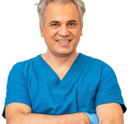 Bărbat cu părul cărunt, îmbrăcat în halat albastru, zâmbind și având mâinile încrucișate.