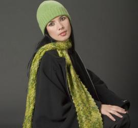 Femeie purtând o pălărie verde și o eșarfă verde, zâmbind în fața unui fundal întunecat.