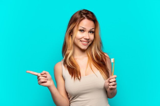 Tânără cu păr lung și blond, ținând o periuță de dinți și arătând cu degetul spre o parte.