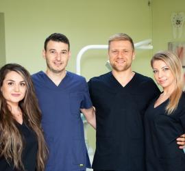 Patru medici dentiști îmbrăcați în uniforme medicale, zâmbind în fața camerei.