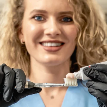 O persoană cu păr creț ținând o periuță de dinți și un tub de pastă de dinți în mâini.