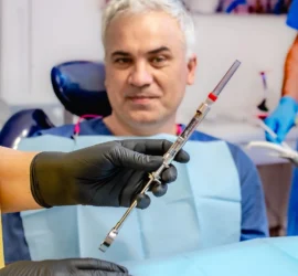 Pacient aflat pe fotoliul dentar se uita cu anxietate la seringa cu anestezic